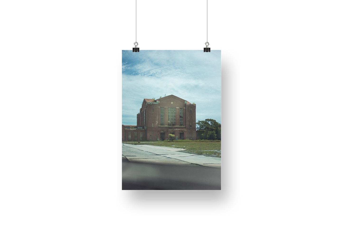 Poster of a building with a blue sky and clouds, hanging on a white wall.