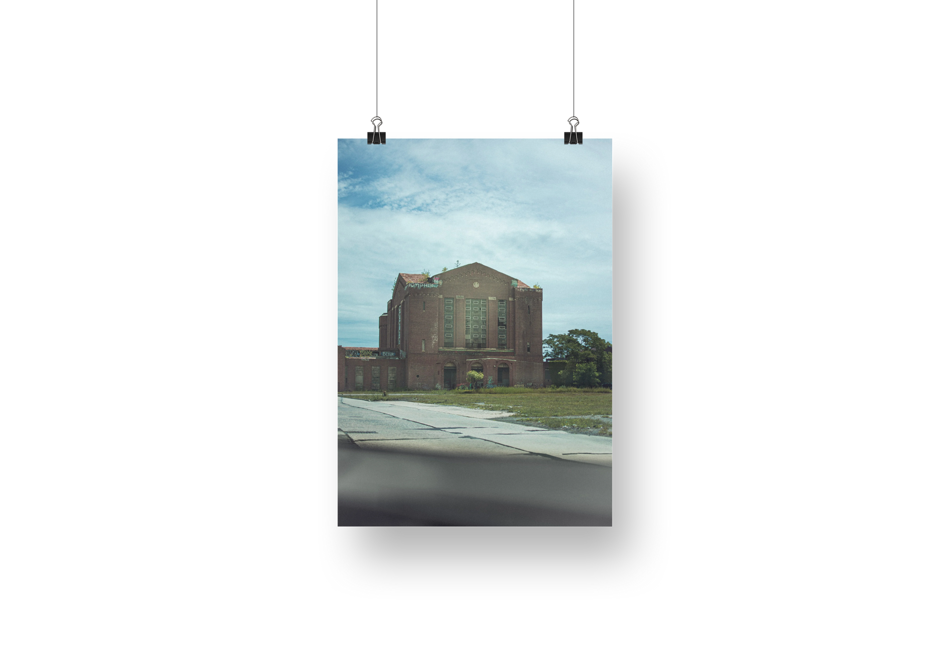 Poster of a building with a blue sky and clouds, hanging on a white wall.